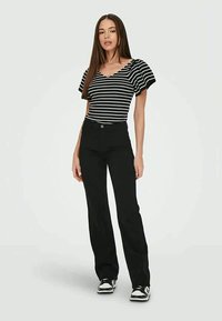 Calças de flair pretas combinadas com uma blusa de manga curta em preto e branco com riscas, apresentando um tecido texturizado e um design de manga levemente bufante.