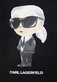 Black fabric features a cartoon-like illustration of a figure in a black suit and oversized sunglasses, with white hair and text reading "Karl Lagerfeld."