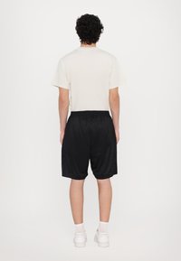 T-shirt blanc à manches courtes associé à un short noir avec cordon de serrage, présentant une texture lisse et une longueur jusqu'aux chevilles. Des baskets blanches complètent le look.