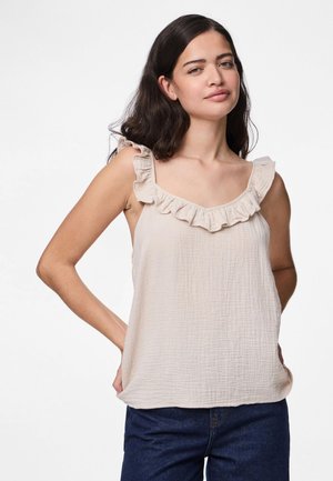 Haut sans manches beige clair avec un tissu texturé et un décolleté à volants. Coupe décontractée avec un ourlet droit, associé à un jean bleu foncé.