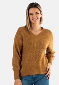 Suéter de cuello en V y mangas largas en un cálido color marrón con un patrón de espiga texturizado, puños y cinturilla acanalados, combinado con jeans azules.