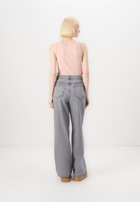 Top sin mangas de color rosa claro con un acabado texturizado, combinado con jeans grises de talle alto y pierna ancha que cuentan con bolsillos traseros y una cintura elástica.