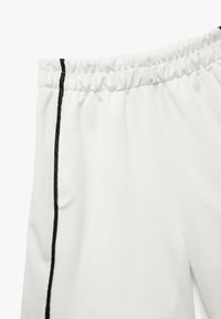 Hvide sportbukser med en tekstureret overflade. Har en sort sideliste og en elastisk talje for justerbarhed.