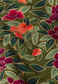 Tela floral con fondo verde, con flores moradas y naranjas, hojas verdes y contornos beige. La textura parece suave y tejida.