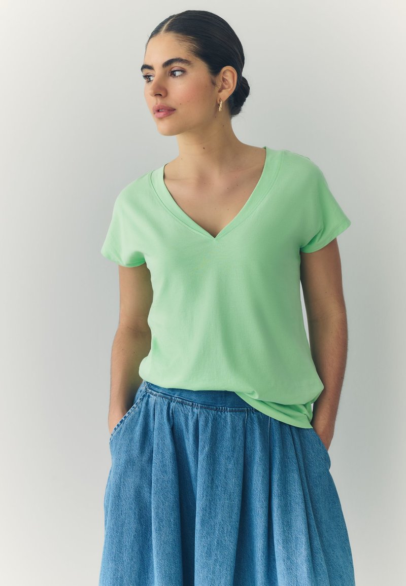 Heleroheline V-kaelusega t-särk, mis on valmistatud pehmest kangast, kombineeritud sinise teksaseelikuga, millel on voldid ja taskud.