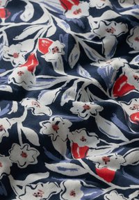 Kokvilnas audums ar ziedu rakstu baltā un sarkanā krāsā uz tumši zilas fonā, ar gludu tekstūru un dažādiem lapu dizainiem.