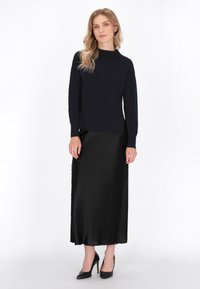 Pulover tricotat de culoare bleumarin cu un gât înalt, asortat cu o fustă maxi din satin negru neted și pantofi cu toc înalt negri.