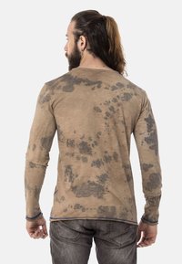 Langarmhemd in hellem Beige mit einem Spritzmuster in Dunkelgrau. Weicher Stoff mit entspannter Passform und kontrastierenden blauen Nähten.