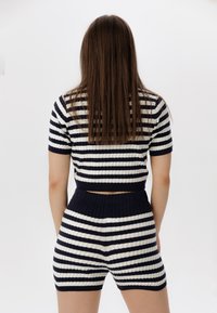 Pletený dvoudílný outfit v námořnické modré a krémových pruzích. Obsahuje přiléhavý crop top a šortky s vysokým pasem, ribbovanou texturou a elastickým pasem.