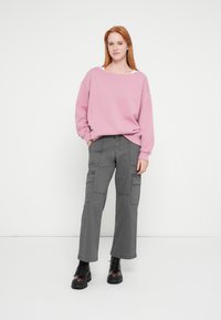 Rózsaszín, túlméretezett pulóver lehorgonyzott vállakkal, laza szürke cargo nadrággal oldalzsebekkel párosítva. A megjelenést fekete fűzős csizmák egészítik ki.