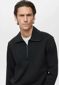 Sudadera negra de cuello alto y media cremallera. Fabricada con una tela suave y cálida, con un corte relajado. Diseño simple, sin patrones.