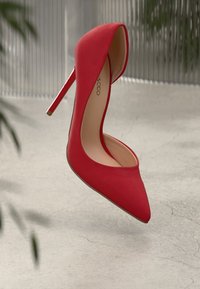 Červená vysoká bota na podpatku vyrobená z hladkého materiálu, s špičatou špičkou a elegantním siluetou. Podpatek je ve stylu stiletto s zlatým akcentem.