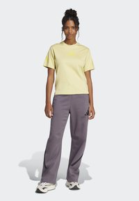 Světle žluté tričko s krátkým rukávem a malým žlutým logem, spárované s volnými šedými tepláky se černými akcenty a logem.
