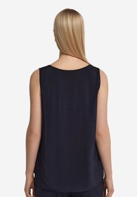 Marinblå ärmlös topp med rund halsringning, slät textur och en mjukt rundad nederkant. Bakvyn framhäver axeldetalj och passform.