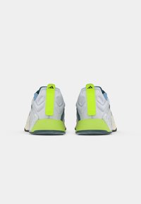 Chaussures de sport avec une tige en maille gris clair, des accents bleus, une languette et une semelle vert fluo, présentant des motifs texturés et un design à profil bas.