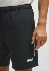 Juodi sportiniai šortai, pagaminti iš lengvos medžiagos, su elastingu juosmeniu, šonine kišene ir baltu "BOSS" logotipu ant kojos.
