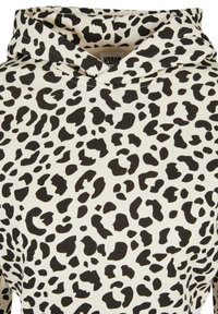 Sweat à capuche blanc avec motif léopard noir irrégulier couvrant le tissu, montrant l'encolure et la zone de la capuche.