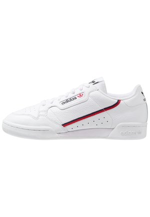 Basket Adidas en cuir blanc à tige basse avec une bande rouge et bleu marine, des perforations sur le côté, et des logos de la marque sur la languette, le côté et le talon.