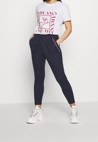 Vit t-shirt med röd grafiktryck, matchad med marinblå slim-fit joggers med sidofickor och röda randiga detaljer. Vita sneakers.