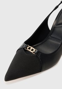 Chaussure slingback noire à bout pointu avec devant en tissu, côtés en cuir, semelle intérieure rembourrée et petit détail de chaîne en or près de l'ouverture du bout.