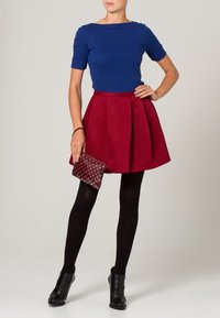 Niebieska bluzka z krótkim rękawem połączona z czerwoną plisowaną spódnicą. Czarne rajstopy i botki za kostkę. Bordowa kopertówka z białymi ćwiekami dopełnia całość.