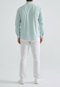 Chemise à rayures vert clair et blanche à manches longues avec un col boutonné, associée à un pantalon blanc et des baskets blanches.