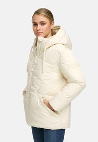 Light cream puffer jacket with a hood, featuring diagonal stitching, zipper front, and front pockets. Accented with rope drawstrings.