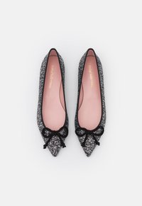 Ett par spetsiga svarta glittriga balettklackar med svarta rosetter och rosa inlägg som är märkta Pretty Ballerinas, visade uppifrån på vit bakgrund.