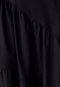 Črna obleka z večnimi nagubami, teksturiranim materialom in diagonalno šivano zasnovo. Gladek videz z izrazitim nabranim detajlom na robu.