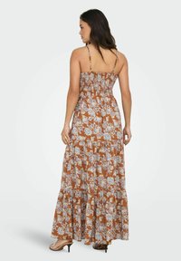 Maxi kjole i brun med blomstermønster. Har tynde justerbare stropper, smocked liv og lagdelt flæsefor. Glat, letvægtsstof.