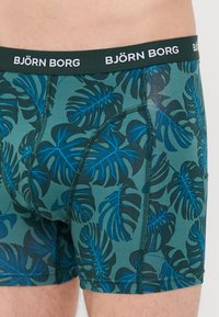 Grüne Boxershorts mit einem dunkelblauen und türkisfarbenen tropischen Blattmuster. Elastischer Bund mit dem deutlich sichtbaren "BJÖRN BORG"-Logo.
