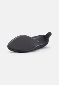 Semelle d'une chaussure plate en daim bleu marine avec petit talon, montrant une semelle extérieure en caoutchouc à texture lisse et une indication de taille sur un fond blanc.
