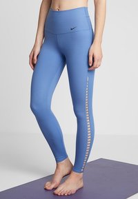 Leggings blu a vita alta con una texture liscia, dotati di un pannello in mesh laterale con design a ritaglio. Logo Nike sopra l'elastico.