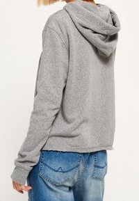 Sudadera con capucha gris, hecha de tela suave, con puños acanalados, diseño cropped, combinada con jeans azules desgastados que presentan bolsillos traseros distintivos.