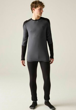 Young man wearing a fitted gray and black long-sleeve top with matching black leggings and socks standing against a plain background.