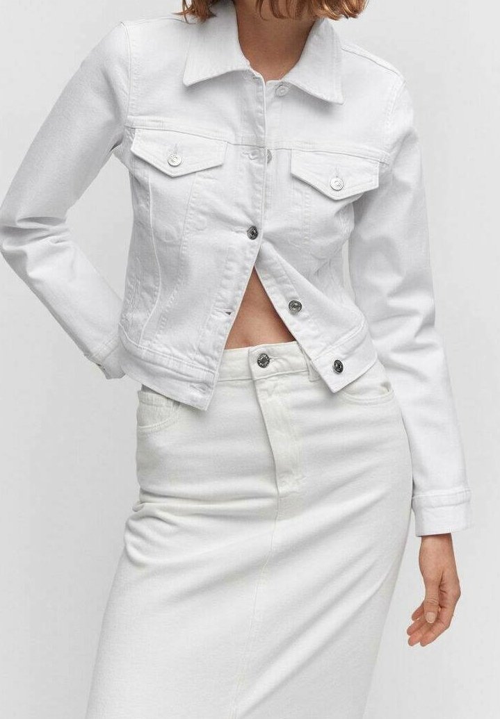Giacca di denim bianca con due tasche frontali, bottoni argentati e colletto. Indossata su una gonna bianca coordinata. Texture liscia.