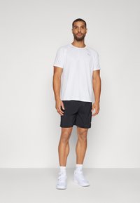 Conjunto atlético para hombres que incluye una camiseta blanca de secado rápido y pantalones cortos negros, complementados con zapatillas blancas. Diseño simple y funcional.