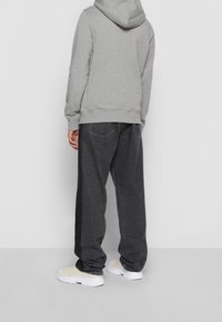 Grijze hoodie met een voorste kangoeroezak, gecombineerd met baggy zwarte spijkerbroek. Witte sneakers maken de casual outfit compleet.