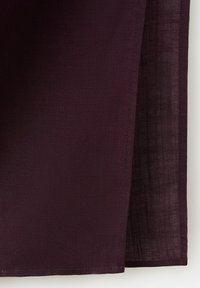 Tissu violet foncé avec une texture tissée subtile, plié pour montrer des couches superposées et des bords cousus.