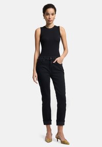 Schwarzes, geripptes, ärmelloses Oberteil kombiniert mit eng anliegenden schwarzen Jeans mit umgeschlagenen Bündchen und gemusterten gelben Absätzen. Schlichtes Design mit klassischer Silhouette.