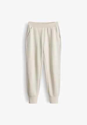 Crèmekleurige joggingsbroek met elastische tailleband, zijzakken en geribbelde boorden op een witte achtergrond.