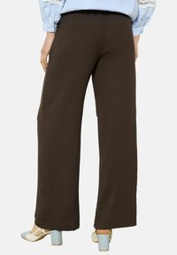 Brown wide-leg pants made of soft material with an elastic waistband, featured on a model paired with light blue block-heeled shoes.