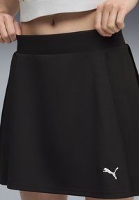 Jupe de sport noire en matériau lisse et extensible. Dotée d'une large ceinture et d'un logo Puma blanc au bas à droite.