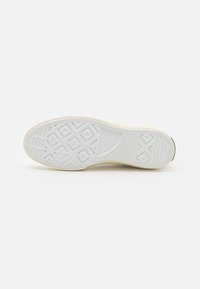 Podešev bílé tenisky Converse All Star, na které jsou viditelné vzory v diamantovém a pruhovaném tvaru, s vyraženým logem značky poblíž paty.