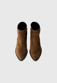 Bottines en suède marron avec un bout pointu et une fermeture éclair sur le côté, présentées de dessus sur un fond gris clair.