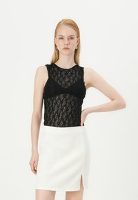 Débardeur en dentelle noire avec un motif en diamant, associé à une mini jupe blanche avec une fente sur le côté. Tissu lisse, design ajusté.