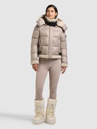 Giacca imbottita beige con colletto in shearling, due tasche frontali e chiusura nera. Abbinata a leggings color nudo e stivali invernali bianchi.