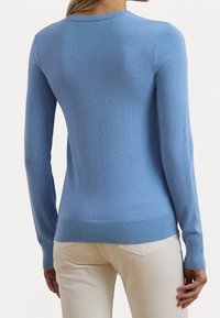 Ljusblå stickad tröja med lång ärm, rund halsringning och ribbad nederkant. Mjuk textur med en figurnära stil. Synlig sömnad på ärmarna.