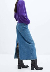 Person wearing a purple sweater, blue denim midi skirt with back slit, and black heeled knee-high boots standing sideways.