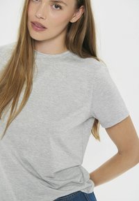 Szara koszulka z krótkim rękawem wykonana z miękkiego materiału, z okrągłym dekoltem, o luźnym kroju i delikatnej strukturze.